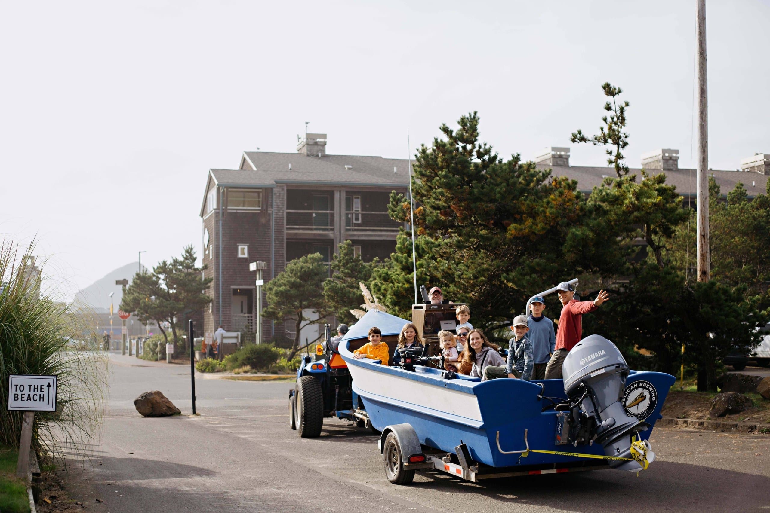 A boat float being pulled by a tractor with a bunch of kids and family for Hart's Camp Events Dory Boat Ride