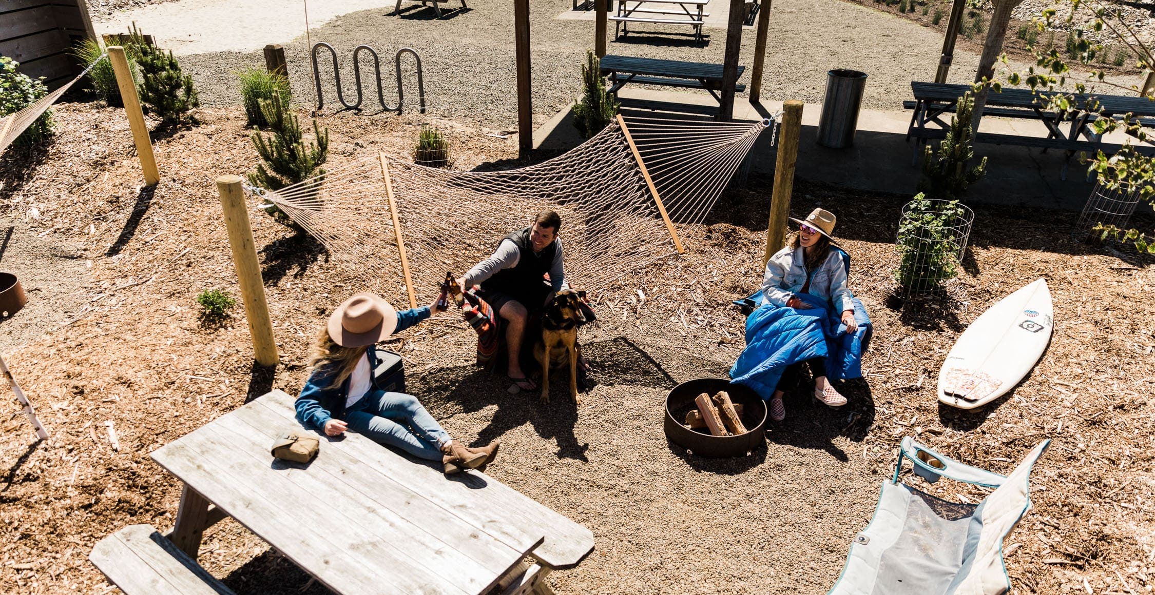 Three people and a dog hanging out on a hammock, picnic table and camping chair in an RV site at Harts Camp