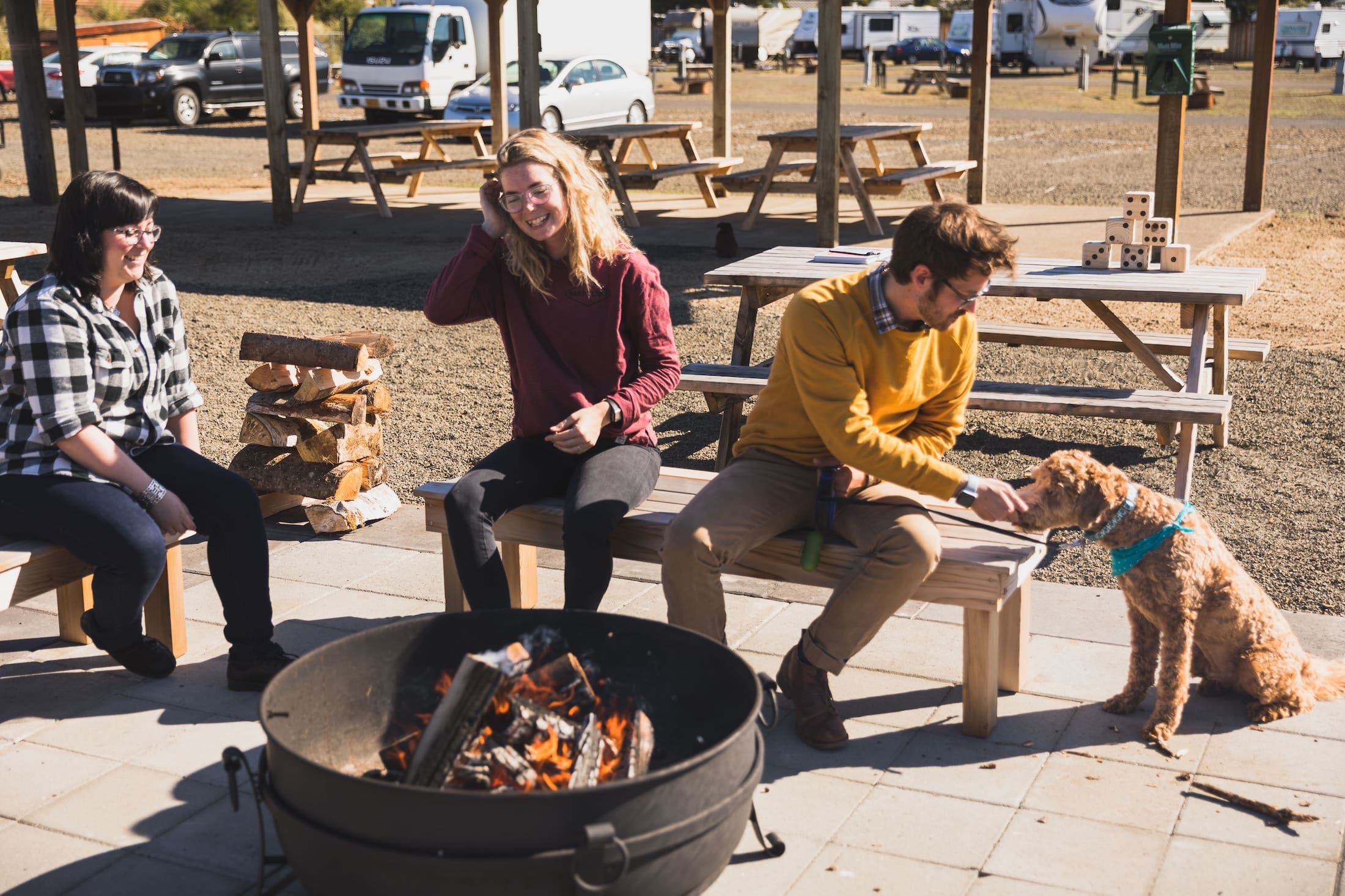 Three people sitting by a fire pit with a golden doodle at Hart's Camp