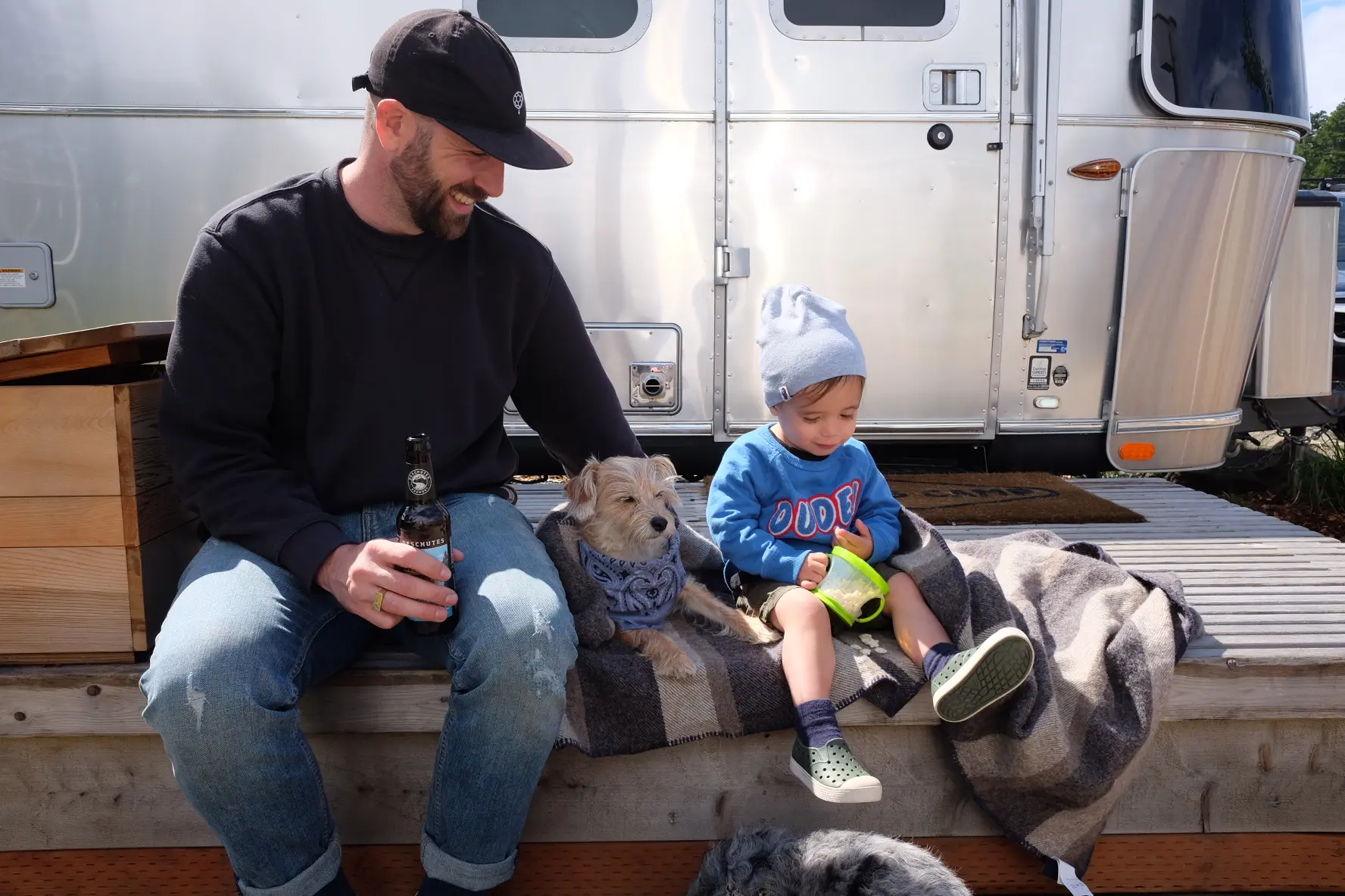 A father, dog, and child sitting on the deck of an airstream at Harts Camp